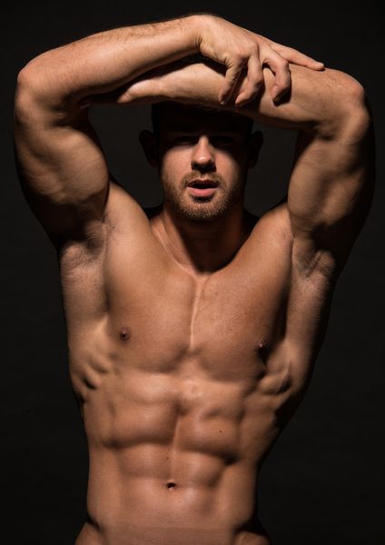A shirtless male model posing with his arms raised