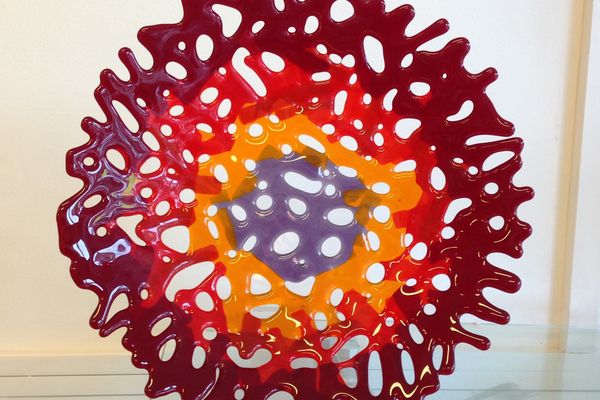 A red, orange and purple fused glass coral bowl on a clear stand