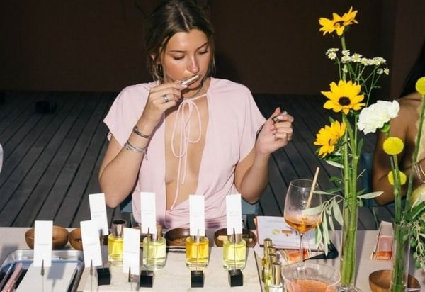 A friend in pink smelling a scent strip at a perfume table with flowers and a cocktail