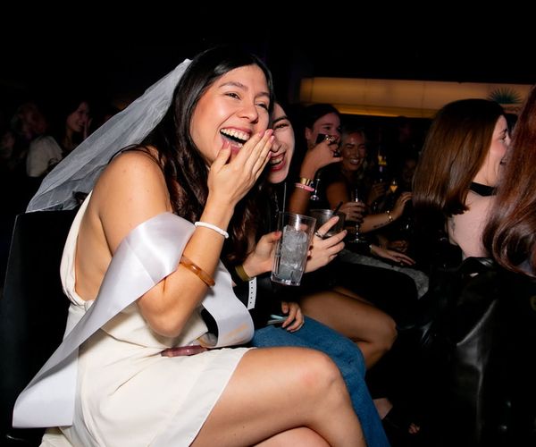 The bride in a veil and sash laughing with her friends in the audience at the show
