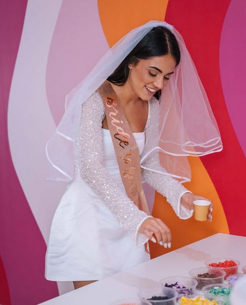A bride to be in a veil and sash at a colourful craft table