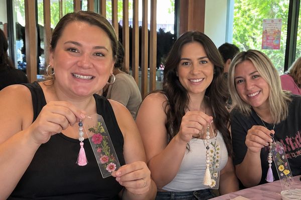 Three smiling friends hold up the pressed flower bookmarks they made