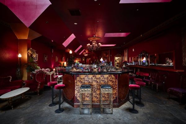 A plush cocktail lounge in deep red with velvet stools and a central bar