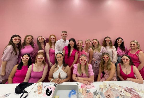 A large hens group in pink and heart sunglasses posing at a workshop table
