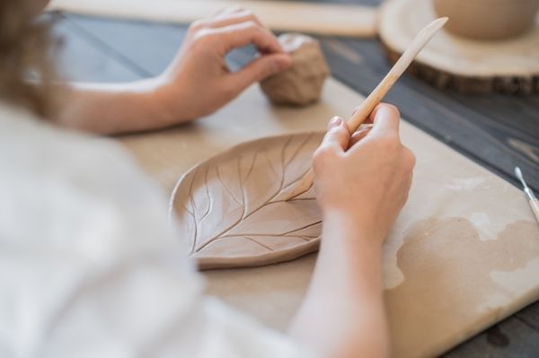 Hen meticulously polishes her leaf-shaped plate with a brush at the clay pottery workshop