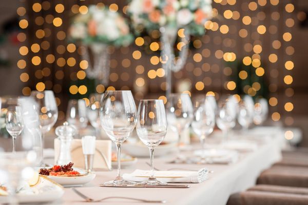 A long dining table set with wine glasses and flowers under warm lights