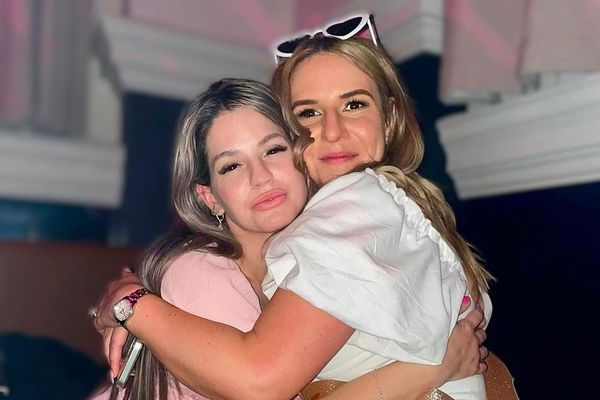 Two friends in pink and white hugging tight, one wearing a glittery bride sash