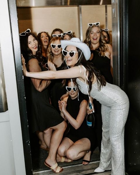 A hens group in heart sunglasses crowding a doorway, the bride to be in a white cowboy hat