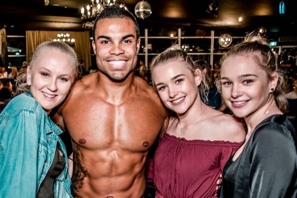 Shirtless waiter in the middle of three smiling friends at a night venue