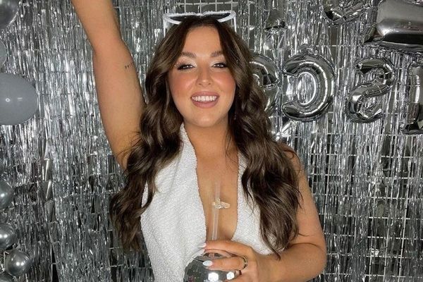 Hen in a white jumpsuit holding a disco ball in front of silver tinsel