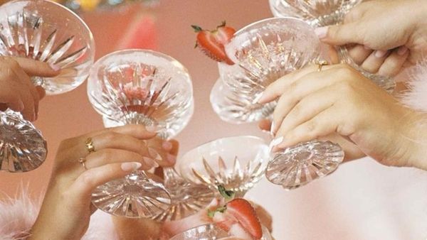 Hands clinking cut glass coupes of pink cocktail with strawberries