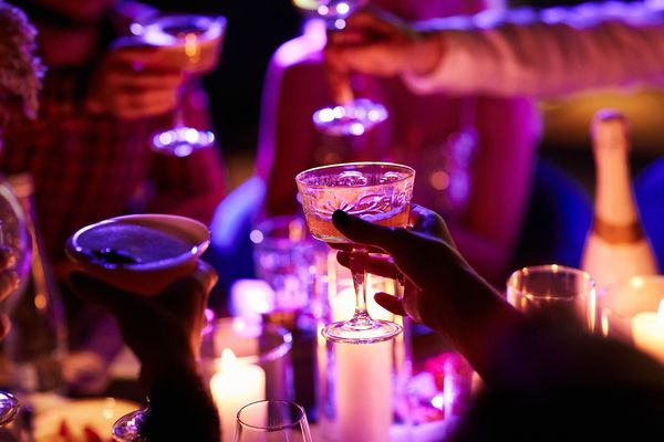 Glasses raised in a toast under purple candlelight