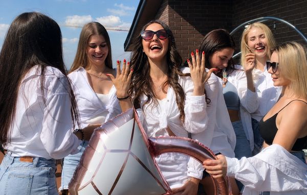 Friends in white laughing as the bride to be shows off her ring