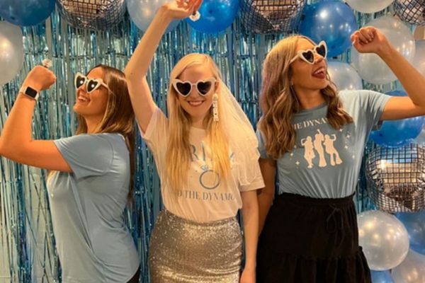 Three friends in heart sunglasses dancing in front of blue tinsel and disco balloons