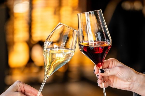 Two hands clinking a glass of white wine and a glass of red