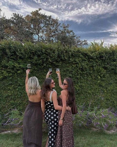 Three friends raising glasses of wine in front of a tall green hedge