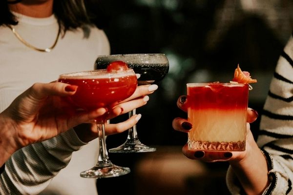 Friends clinking a red cocktail and a layered sunset cocktail