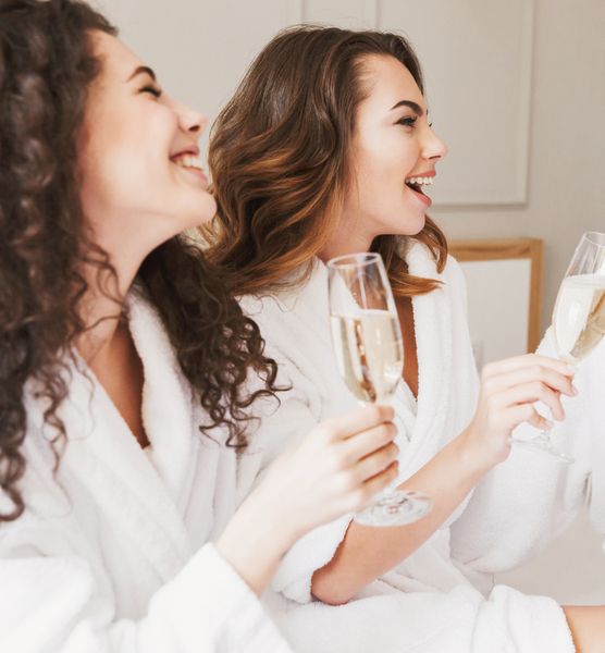 Two friends in white robes laughing with glasses of bubbles