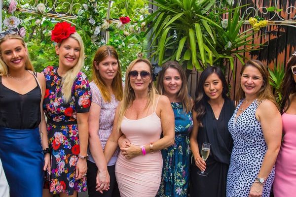Hens group of eight women in dresses posing together on a leafy rooftop terrace