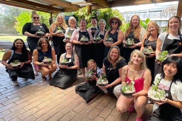 A big group of friends kneels and stands holding their finished glass terrariums