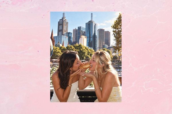 Two friends laughing as they bite into one pastry together, the Melbourne skyline behind them