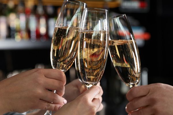 Hands raise three flutes of sparkling wine in a toast at a bar