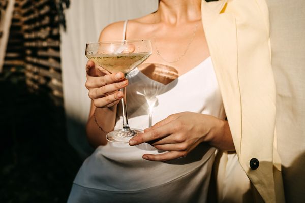 A woman in a white slip and cream blazer holding a coupe of bubbles