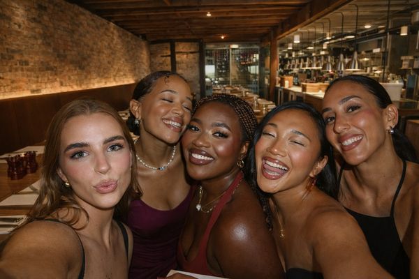 Five women squeezed together for a smiling group selfie inside a warm brick bar