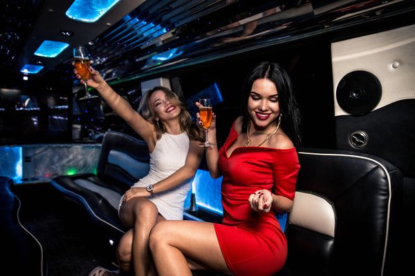 Two lovely ladies are wearing red and white dresses with champagne glasses in hand and enjoying themselves on a luxurious Hummer cruise