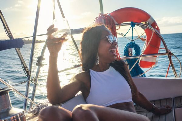 A woman raising a glass on the deck of a sailing boat in the sun