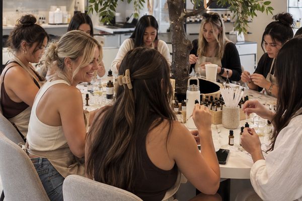 A group of friends blends perfume at round tables under a leafy indoor tree