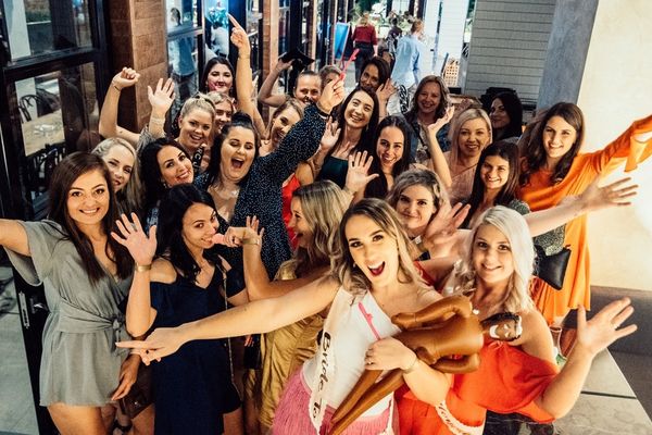 Big group of women cheering with arms out at a riverside bar