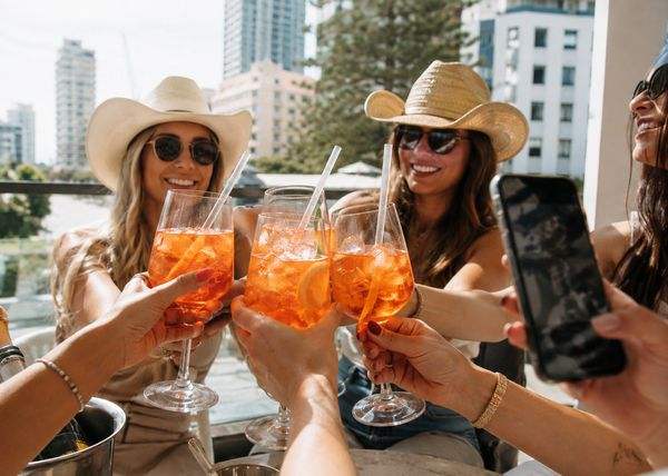 Friends in cowboy hats and sunglasses raising spritz glasses on a sunny rooftop
