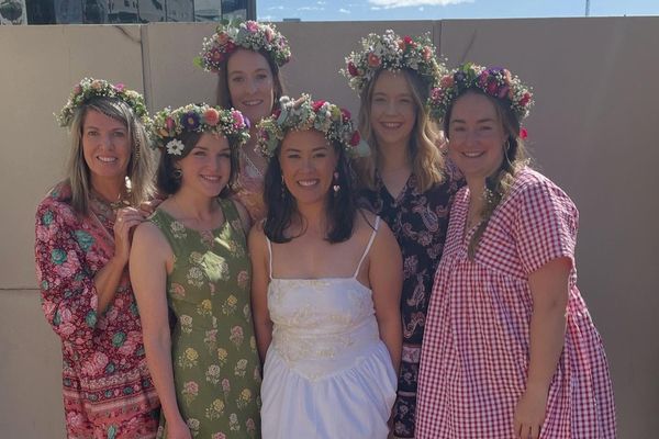 Five friends in fresh flower crowns and summer dresses stand together in the sun