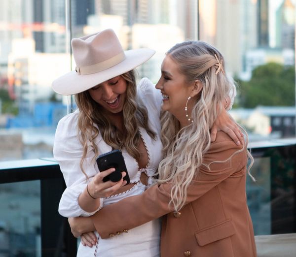 The bride in a hat and white dress hugging her friend on a city rooftop
