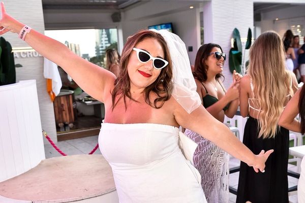Woman in a white dress and sunglasses dancing with arms out on a sunny deck