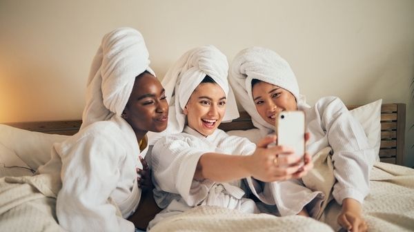 Three friends in white robes and towel turbans laughing at a selfie