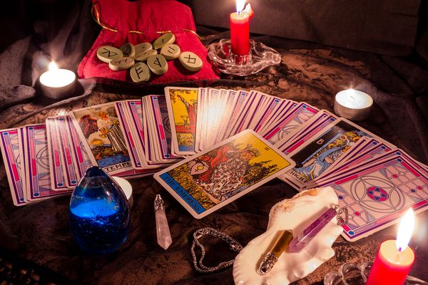 Tarot cards fanned across a table with candles, runes and crystals