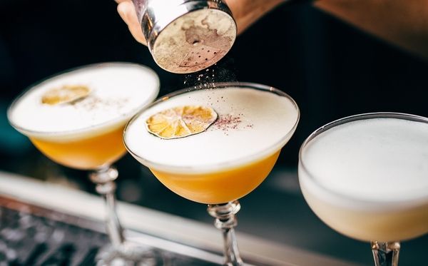 Three cocktail drinks topped with chocolate powder and lemon slices at a bar counter during cocktail making class