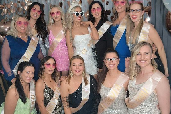Hens in sashes and pink sunglasses gather around the bride before rose gold hearts
