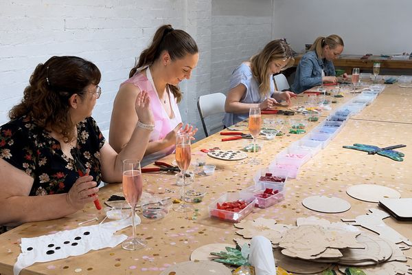 Guests working on mosaics along a long studio table with glasses of pink bubbly