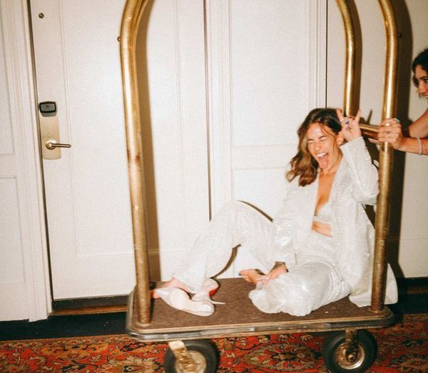 The bride in white sequins laughing as she rides a luggage trolley down the hallway