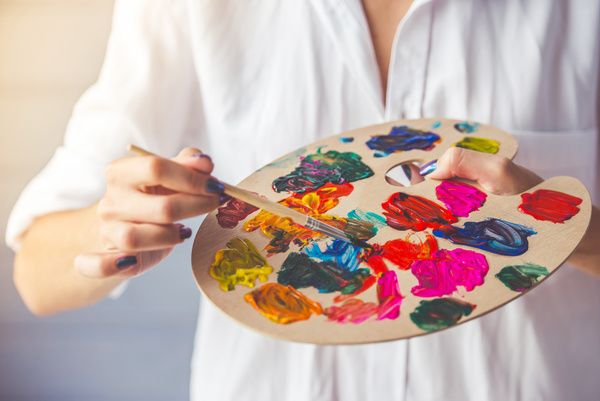 A gorgeous hen is holding a palette and mixing paint colours during a painting workshop in a private studio