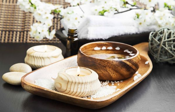 Candles, bath salts, a wooden bowl and white towels set out for a spa treatment