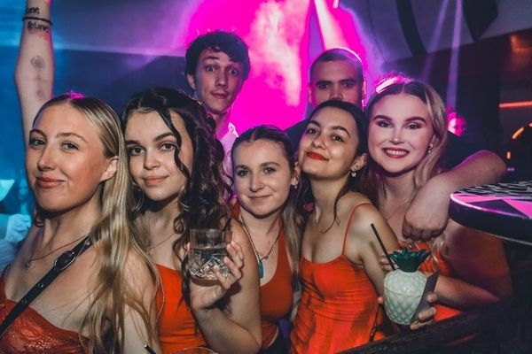 Friends in matching orange dresses squeeze in for a photo under pink lights