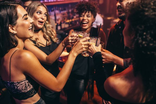 Friends laughing and clinking cocktails in a busy bar