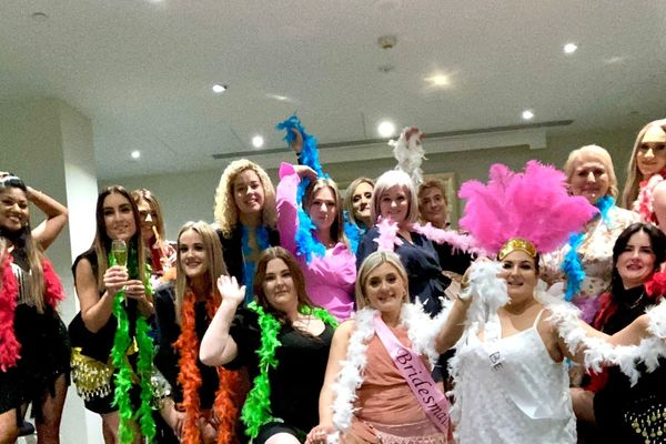 Hens group waving colourful feather boas with a pink feather headdress in a function room