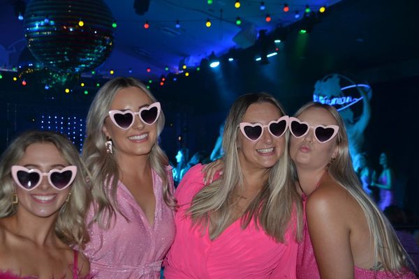 Four friends in heart sunglasses under a disco ball and coloured party lights
