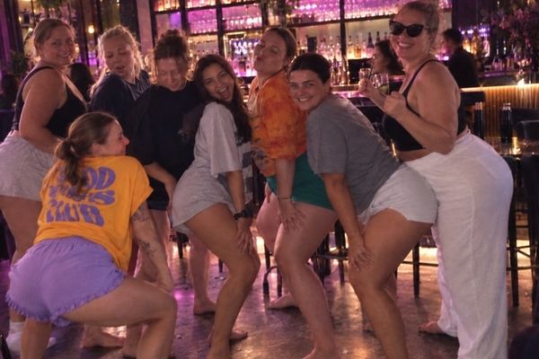 Hens in comfy shorts and tees laugh through a twerk routine in a lounge