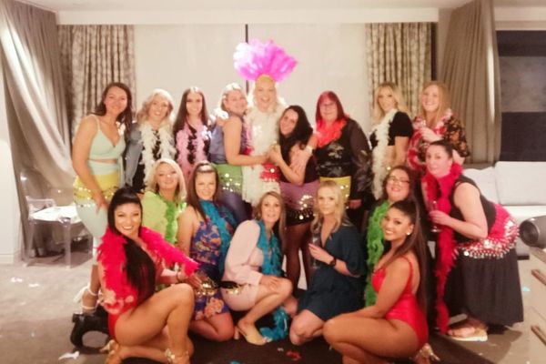 Hens group in colourful feather boas posing together in a bright function room